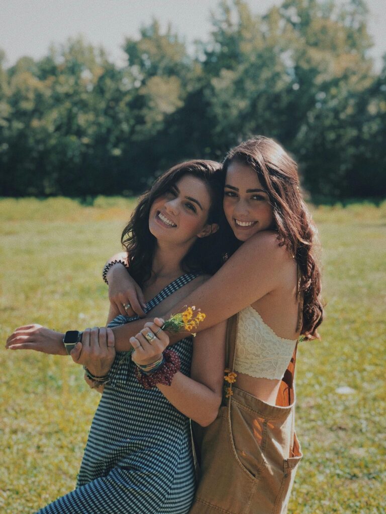 Two smiling sisters embracing in a sunlit park, enjoying a warm summer day together. | online clothing stores
