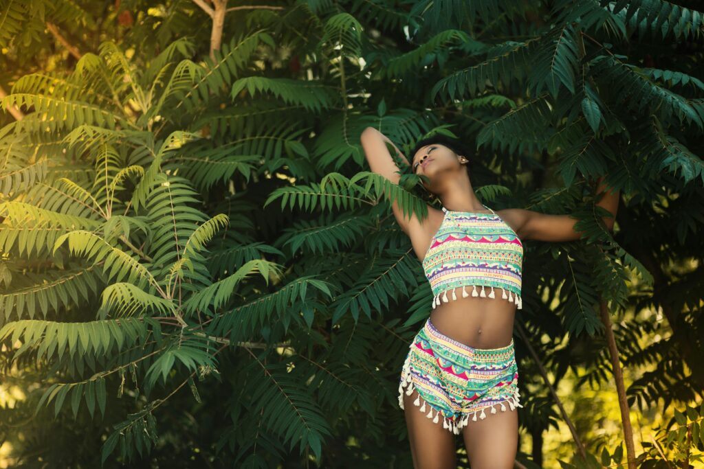 Woman posing in colorful summer attire among lush green foliage, showcasing fashion outdoors. | summer outfits